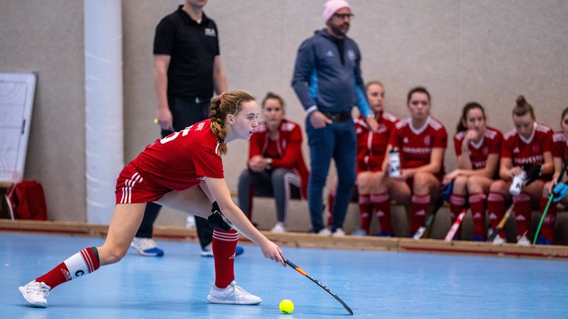 Hockeyspielerin Natalie Hoppe am Ball, hinter ihr steht BHC-Trainer Florian Keller vor der Ersatzbank mit den Bremer Spieleroinnen.