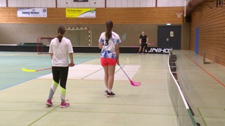 Vier Mädels, die in einer Turnhalle Hokey spielen.