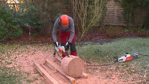 Ein Mann bearbeitet ein Stück Holzstumpf mit einer Kettensäge.