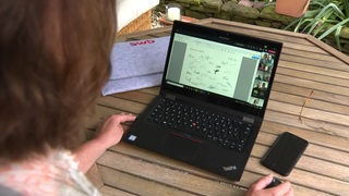 Eine Frau sitzt an einem Gartentisch vor ihrem Laptop um im Homeoffice zu arbeiten. 