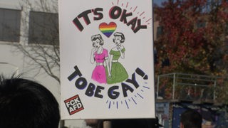 Auf einem Plakat, bei der Demonstration gegen trans- und queerfeindliche Gewalt, steht "It´s okay to be gay!".