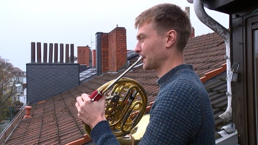 Ein Mann steht auf einem Balkon und spielt Horn.