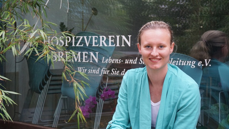 Eine junge Frau sitzt vor einem Fenster mit der Aufschrift "Hospizverein Bremen"