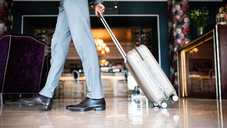 Ein Mann geht durch eine Hotellobby und zieht dabei einen Koffer hinter sich her.