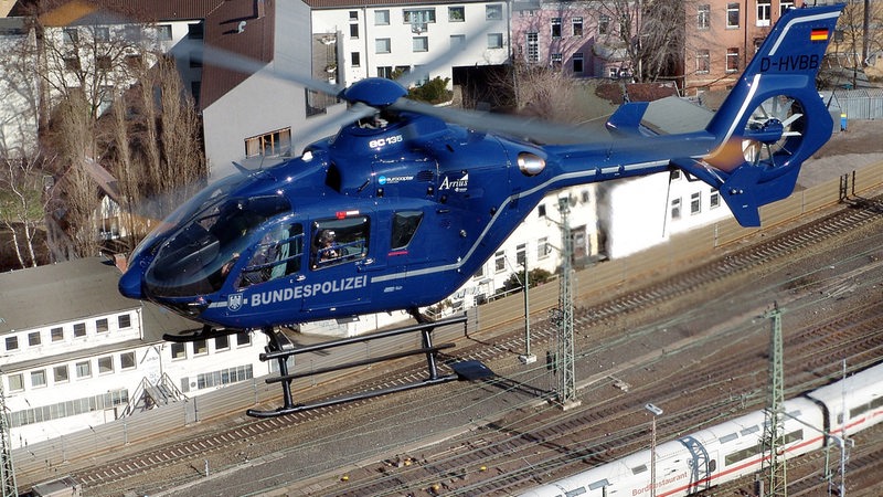 Ein Blauer Hubschrauber fliegt über Bahngleisen.