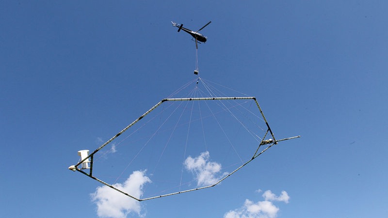 Ein Hubschrauber fliegt im Himmel und zieht ein sechseckiges Gestell 