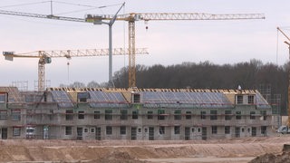 Ein Neubaugebiet in Huckelriede am Werdersee. Häuser im Rohbau sind auf der Baustelle zu sehen, dahinter stehen Kräne. 