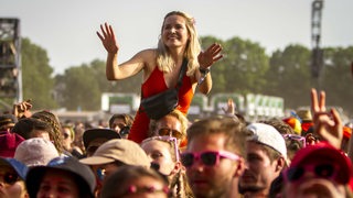 Eine Frau tanzt auf den Schultern einer anderen Person beim Hurricane-Festival