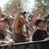 Menschen stehen vor einer Bühne und hören einem Konzert zu.