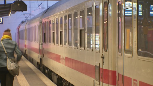 Ein ICE der Deutschen Bahn in einem Bahnhof. Links läuft eine Frau über den Bahnsteig.