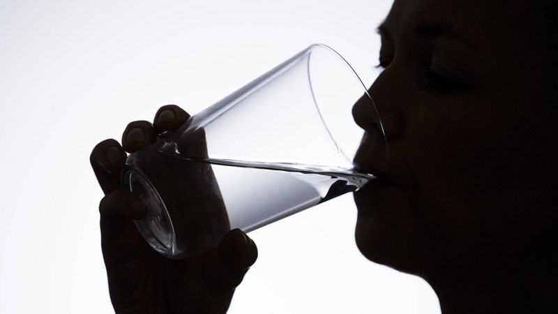 Eine Person trinkt aus einem Wasserglas.