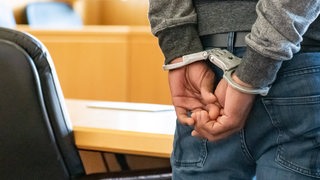 Ein Angeklagert steht im Handschellen in einem Gerichtssaal. 