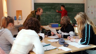 Ein Lehrer gibt mehreren Schülerinnen und Schülern Unterricht