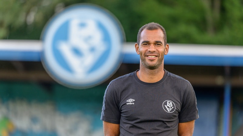 Der Trainer des Bremer SV Benjamin Eta posiert im Stadion am Panzenberg lächelnd für ein Foto.