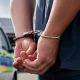 Ein Mann steht in Handschellen vor einem Polizeiauto.