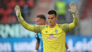 Werder-Torwart Michael Zetterer steht mit erhobenen Händen und konzentriertem Blick auf dem Spielfeld.
