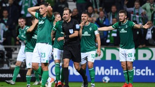 Werder-Spieler umringen den Schiedsrichter entgeistert und mit ungläubigen Gesten.