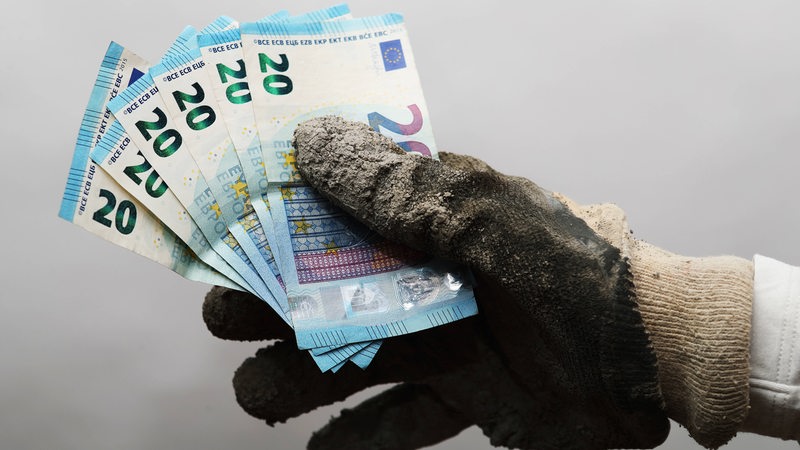 Ein Hand mit dreckigem Handschuh hält 20-Euro-Scheine.