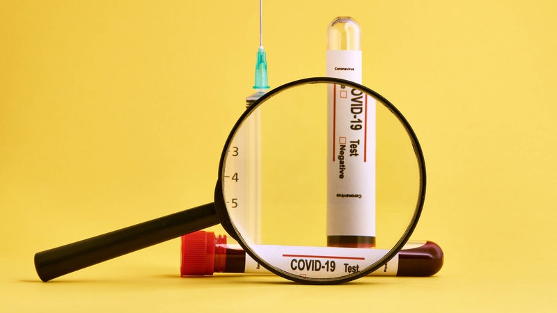 Eine Blut-Ampulle für einen Corona-Test hinter einer Lupe