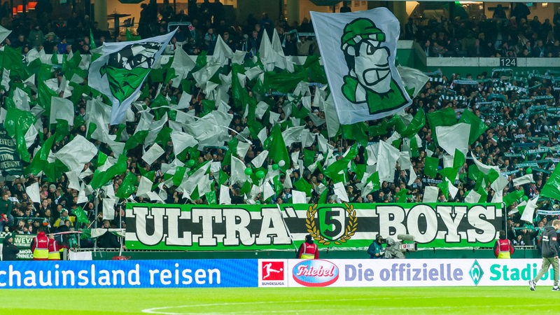 Die Ultras im Weser-Stadion feuern ihr Team an und schwenken grün-weiße Fahnen.