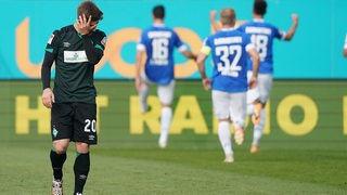Werder-Profi Romano Schmid wischt sich frustriert über das Gesicht, während hinter ihm die Darmstädter Spieler ihr Tor bejubeln.