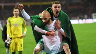 Werder-Spieler Ömer Toprak trägt nach dem Spiel Marvin Ducksch Huckepack, der seine Freude hinaus schreit.