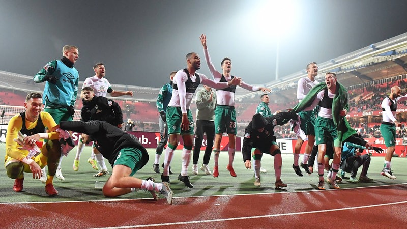 Viele Werder-Spieler feiern den Sieg hüpfend und ausgelassen vor der Fan-Kurve in Nürnberg.