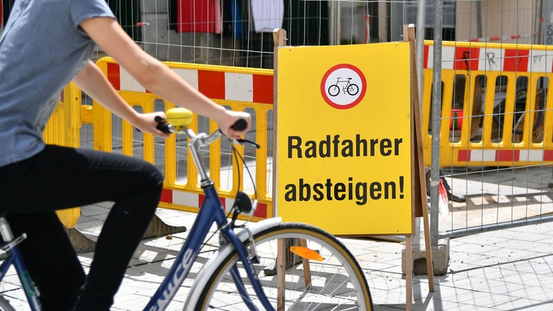 Ein Fahrradfahrer fährt an einem Schild vorbei, auf dem steht: "Radfahrer absteigen".
