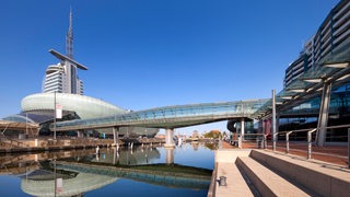 Das Klimahaus und die gläserne Brücke über dem Alten Hafen in Bremerhaven spiegeln sich auf dem Wasser.