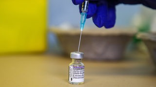 Eine Spritze wird ein Impfstoff-Fläschen gesteckt