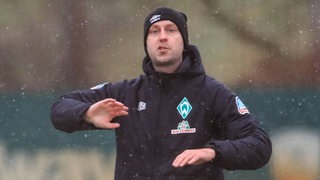 Ole Werner gestikuliert während des Werder-Trainings im Schnee. 