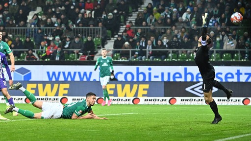 Werder-Spieler Milos Veljkovic liegt nach seinem Torschuss mit der Hacken auf dem Bauch und schaut dem Ball hinterher.