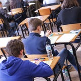 Schüler sitzen hintereinander an Tischen und lösen Aufgaben.