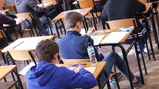 Schüler sitzen hintereinander an Tischen und lösen Aufgaben.