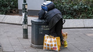 Ein Mann sucht in einer Mülltonne nach Plastikflaschen.