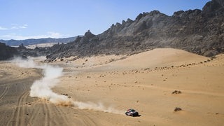 Rallye-Wagen allein auf weiter Strecke in der Wüste am Rande einer Bergkette bei der Rallye Dakar in Saudi Arabien.