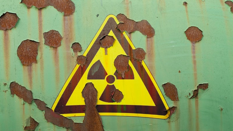 Auf einer grünen, rostigen Wand klebt ein Atomkraft-Zeichen.
