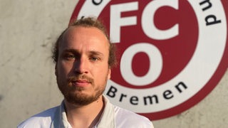 Daniel Prause vor dem Logo des FC Oberneuland