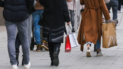 Mehrere Menschen schlendern mit Shopping-Taschen eine Straße entlang.