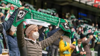 Ein Werder-Fan hält einen Werder-Schal im Stadion hoch.