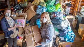 Zwei Frauen stehen vor einem Berg an Spenden.