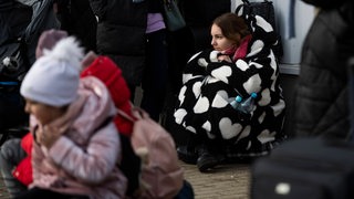 Eine geflüchtete junge Frau sitzt auf dem Boden und wartet.