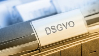 Ein Schild mit der Aufschrift "DSGVO" klemmt in einer Akte.