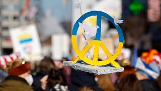 Bei einer Demo ragt ein Peace-Zeichen in die Luft.
