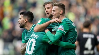 Marvin Ducksch und Anthony Jung umarmen Werder-Torschütze Niclas Füllkrug nach seinem Treffer.