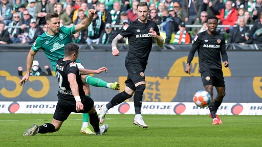 Werder-Stürmer Niclas Füllkrug setzt sich gegen seine Gegenspieler durch und schiebt mit dem rechten Fuß den Ball ins Tor.