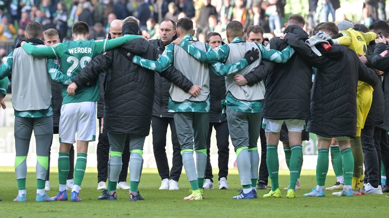 Werder-Spieler stehen nach dem Spiel Arm in Arm am Mittelkreis und umringen Trainer Ole Werner, der eine Ansprache hält.