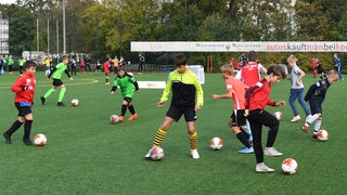 Mehrere Kinder dribbeln beim Fußball-Training mit dem Ball über den Platz.
