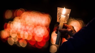 Eine Hand hält eine Kerze in der Dunkelheit.