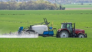 Ein Trecker-Gespann fährt über ein Feld und sprüht Pestizide.